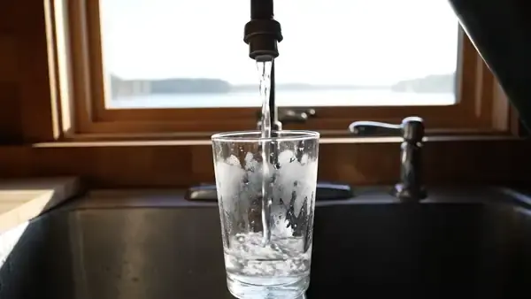 Cold water running from an old faucet into a drinking glass at a cabin sink by a lake window